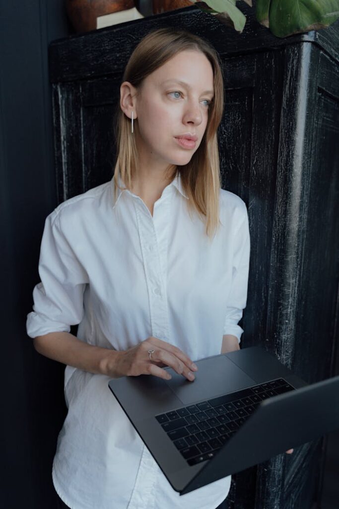 A contemplative woman holding a laptop, embodies modern professional style.
