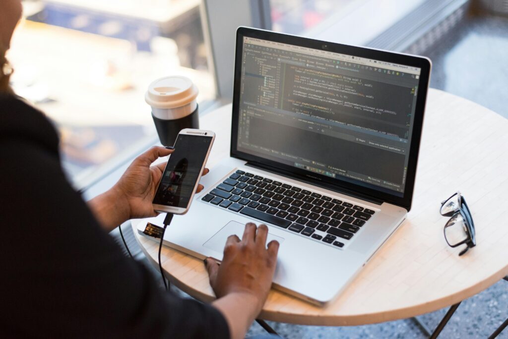 pexels photo 1181244 1181244 Developer working remotely, coding on a laptop with phone in hand, showcasing modern work culture.