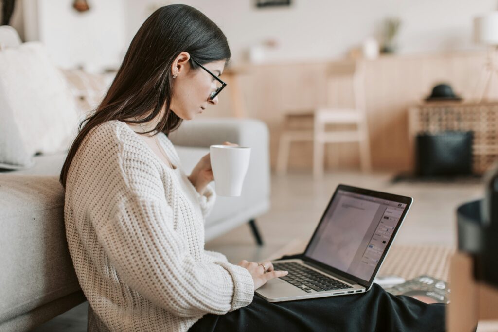 pexels photo 4050350 4050350 Side view of female freelancer in warm sweater and eyeglasses drinking tea from white ceramic cup while sitting on floor near sofa with netbook on legs while creating document for remote work project