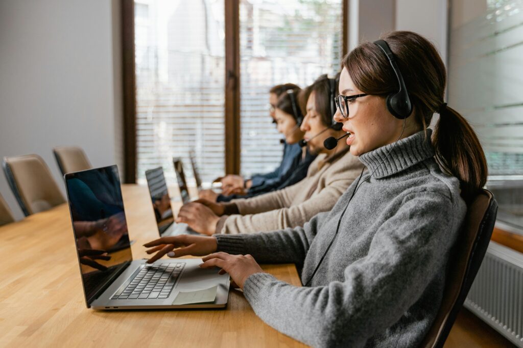 pexels photo 7709146 7709146 Professional customer service team working in a modern office setting with headsets and laptops.