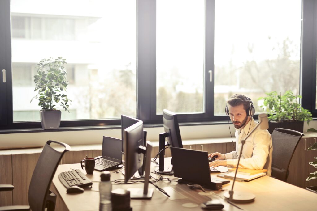 pexels photo 845451 845451 A businessman sits at a desk using multiple computers and a headset in a well-lit modern office.