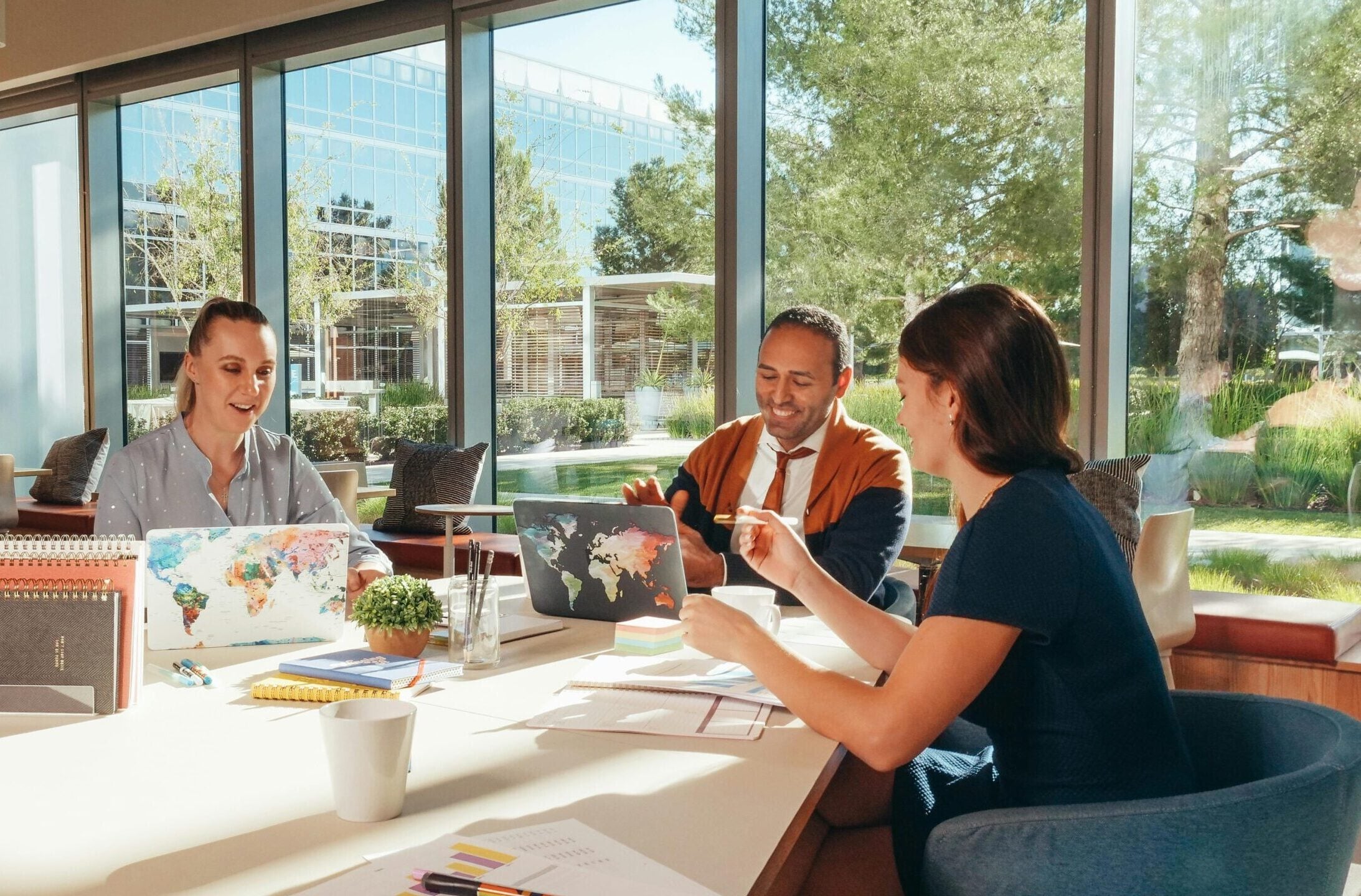Three colleagues brainstorming with laptops in a well-lit office.