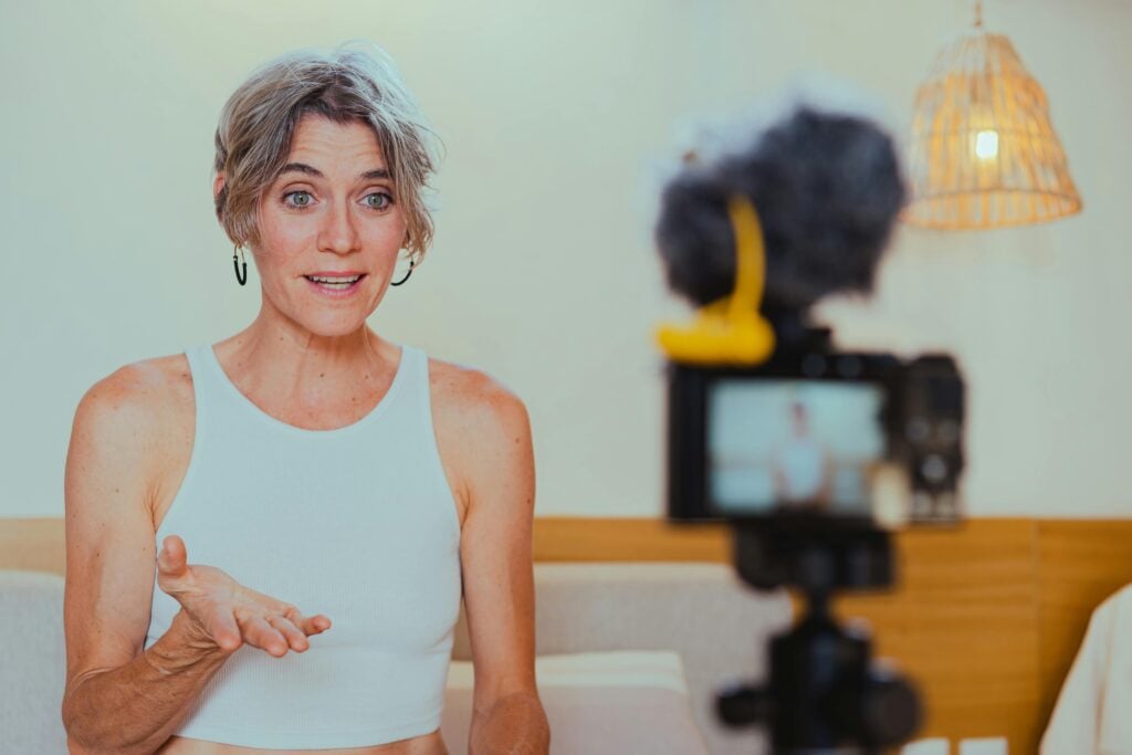 Elderly woman vlogging indoors, engaging with her audience through a camera.