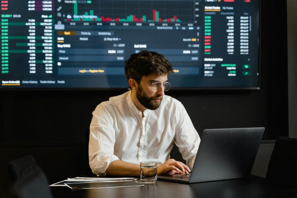 Professional analyzing stock market trends using laptop and digital display in modern office.